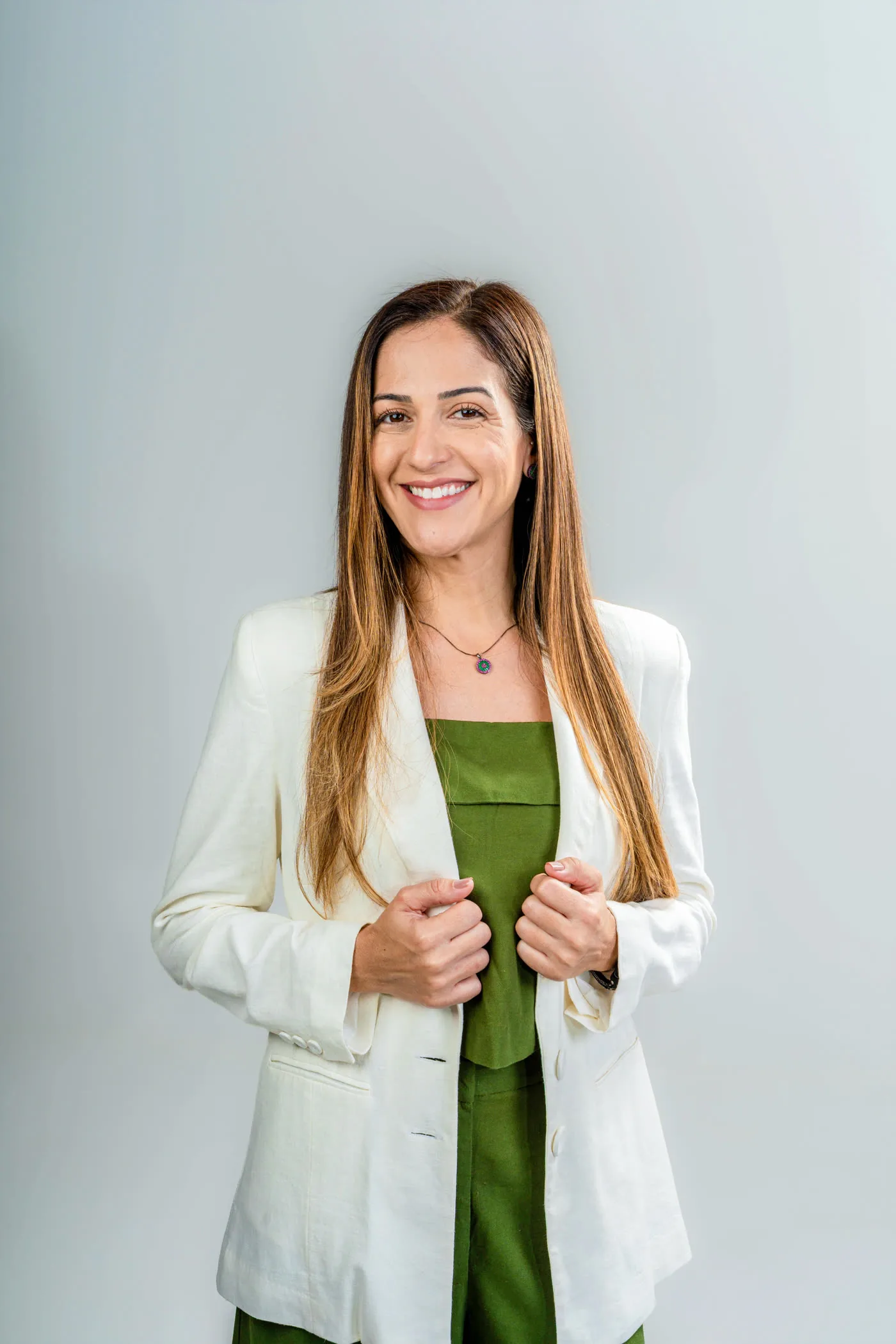 Letícia Canedo, psicóloga, de blazer marfim e blusa verde, sorrindo para a câmera